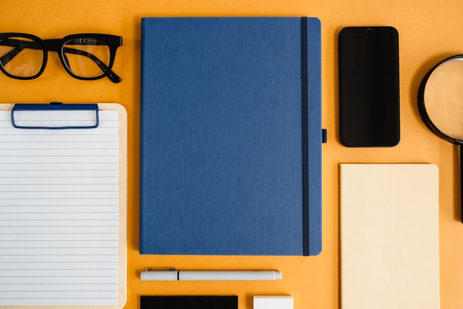 Flat lay of stationery items including notebook, glasses, and smartphone on a vibrant yellow background.